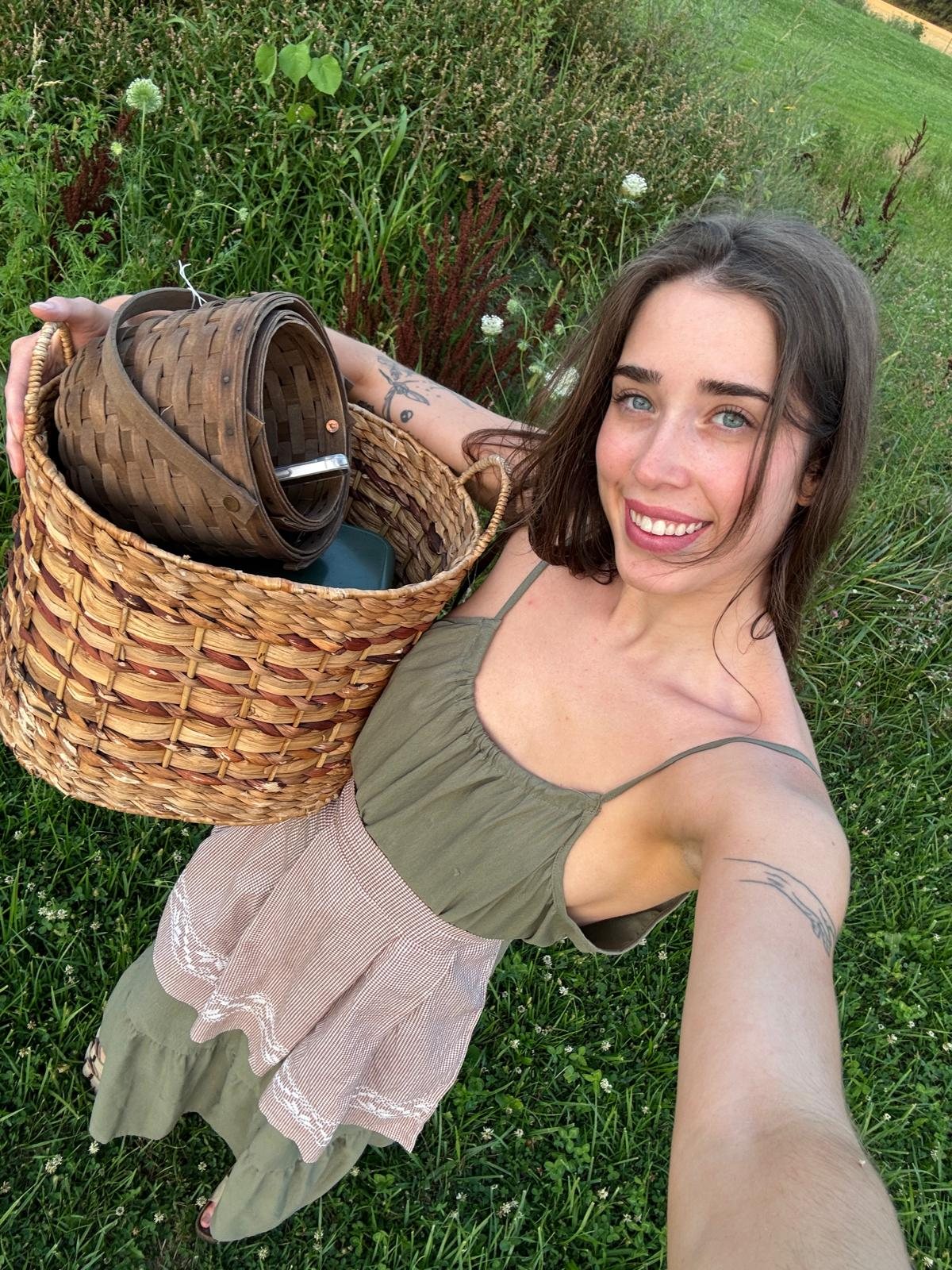 Livinia smiling in a selfie, carrying a woven basket in a grassy field